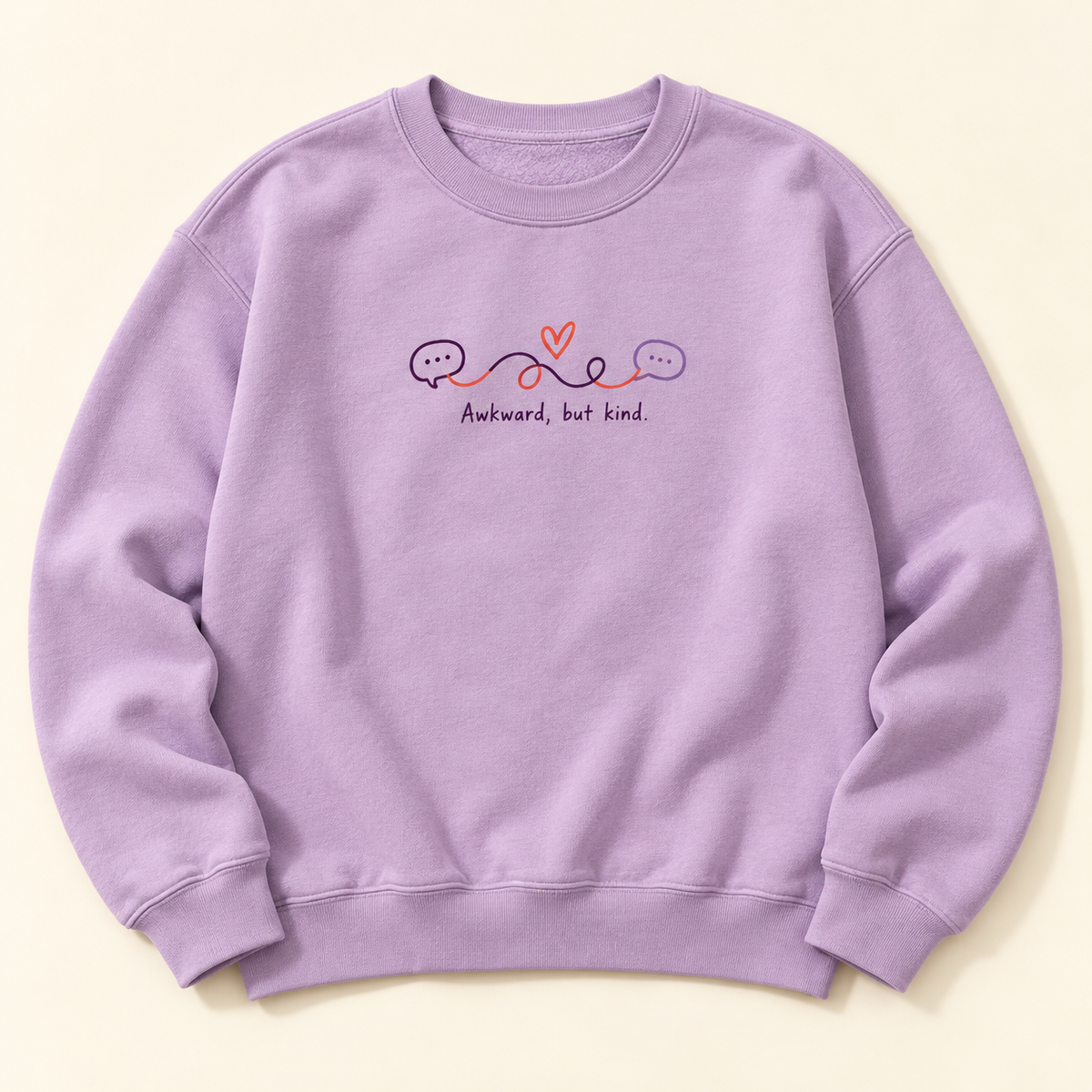 Lavender crewneck with Awkward, but kind lettering, connected speech bubbles, and a coral heart on the chest