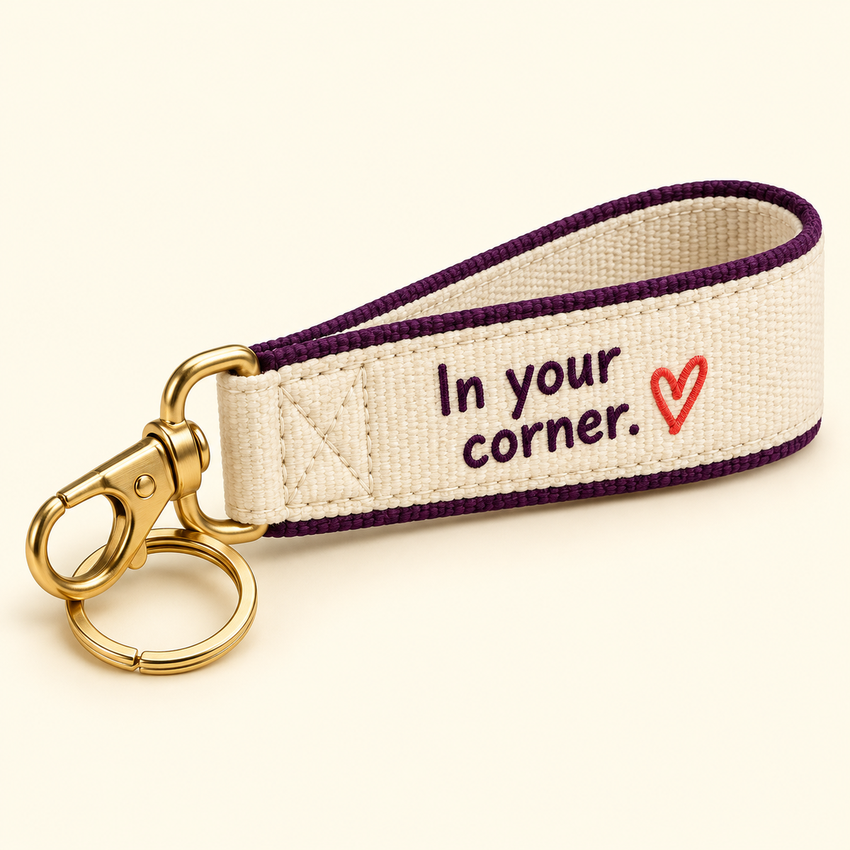 Cream wristlet keychain with plum trim, In your corner lettering, a coral heart, and gold-tone hardware